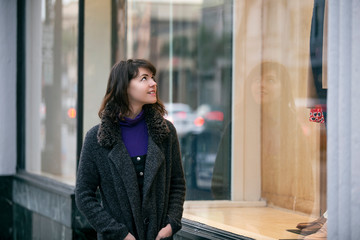 Woman walking outdoors in a city. She is window shopping and looking at a store sale advertising or...
