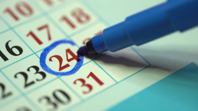 Marking the date in the calendar with a vivid colour using highlighter. Blue highlighting on a paper planner of the twenty-fourth day of the month