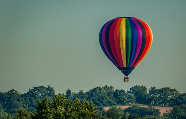 Rainbow colored hot-air balloon floats over the hiltop forest in early morning spring with cloudless sky