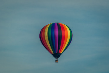 Naklejka premium Rainbow colored hot-air balloon floats over the hiltop forest in early morning spring with cloudless sky