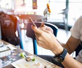 Fototapeta premium Close up of man hand using or looking at his smartphone and having lunch in the restaurant.