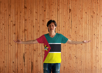 Man wearing Mozambique flag color shirt and standing with arms wide open on the wooden wall...