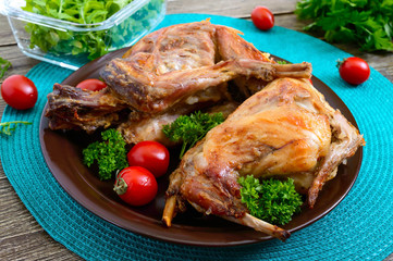 Whole baked rabbit with greens and tomatoes on a plate. Tasty dietary meat.