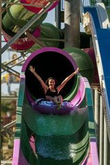 Obraz na płótnie Canvas pretty brunette slim woman with raised hands on a tubing on the rubber ring having fun coming down on the purple water slide in the aqua park. Summer Vacation. Weekend on resort