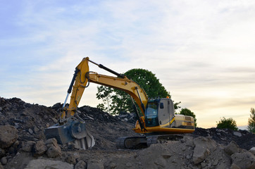 A heavy excavator in a working at granite quarry unloads old concrete stones for crushing and recycling to gravel or cement. Special heavy construction equipment for road construction.