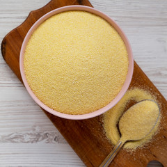 Dry semolina durum flour in a pink bowl over white wooden surface, top view. Overhead, from above, flat lay. Close-up.