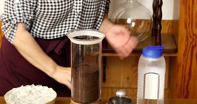 Tapping on glass container with ground coffee to make it flat and putting paper filter on top of coffee 