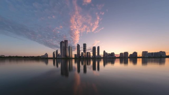 Timelapse of sunset over city skyline shoreline with beautiful colored clouds moving toward viewer. View from water