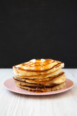 Homemade pancakes with butter and maple syrup on a pink plate, side view. Close-up.