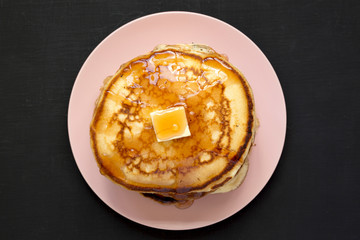 Homemade pancakes with butter and maple syrup on a pink plate, overhead view. Flat lay, top view,...