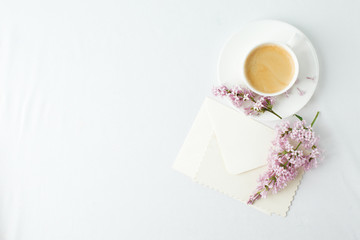 Obraz na płótnie Canvas Minimal elegant composition with coffee cup and lilac branches, envelope on white background, female morning breakfast, woman mother day, saint valentine day