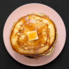 From above, homemade pancakes with butter and maple syrup on a pink plate. Flat lay, top view,...