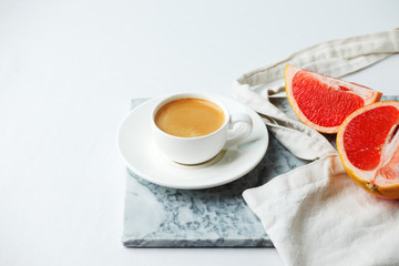 Stylish breakfast concept - cup of coffee, red grapefruit, tissue bag on mafble plate on white background, female modern minimal morning breakfast