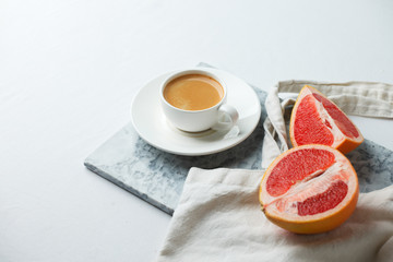 Stylish breakfast concept - cup of coffee, red grapefruit, tissue bag on mafble plate on white background, female modern minimal morning breakfast
