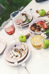 Glasses of white and rose wine, grilled fish plates, vegetables, salad and fruits on the table. Summer party in the backyard. Vertical shot