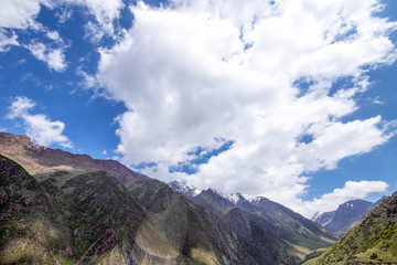 Green hills and mountains with snow-capped peaks against the sky with clouds. Traveling in Kyrgyzstan