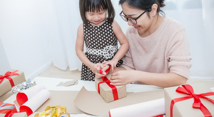 Portrait of happy Asian family little girls help her mother wrapping gift box, celebration holiday...