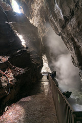 narrow slot canyon gorge with a wild creek and warm steam rising up and a wooden walkway on the side