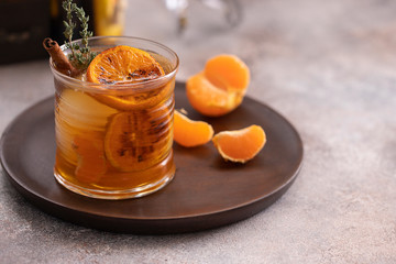 Whiskey sour cocktail with tangerine slices and ice cubes decorated with cinnamon and thyme. Alcohol drink background.