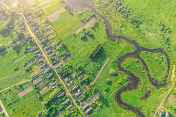 Fototapeta premium Aerial view from the height of the village with houses and streets, plowed fields, meadows, river in the summer.