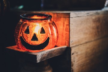Halloween head jack pumpkin glass lantern with burning candle and old wooden table background with copy space.Scary halloween festival holiday concept.