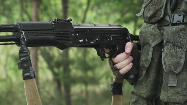Soldier in camouflage reloads the Kalashnikov assault rifle, military action in forest.
