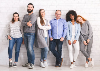 Company of diverse men and women standing at white brick wall