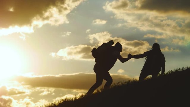 Silhouette of helping hand between two climber. two hikers on top of the mountain, a man helps a man to climb a sheer stone. couple hiking help each other silhouette in mountains with sunlight.