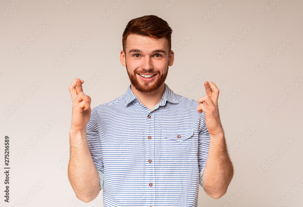 Wall mural positive millennial guy crossing fingers and making wish