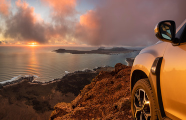 off-road car standing on a rock over a precipice with a view of the ocean and islands