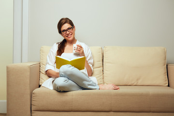 Smiling woman sitting on sofa with open book