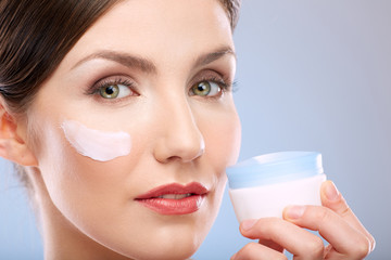 Woman with skin cream on face. Girl holding white jar.