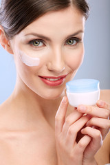 Beauty portrait of woman with clean skin holding cream jar.