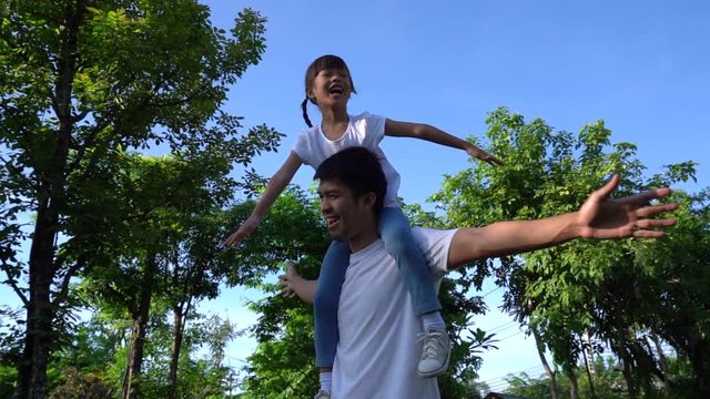 Slow motion of daughter riding on father's neck spinning, laughing happily in the park, Asian family concept