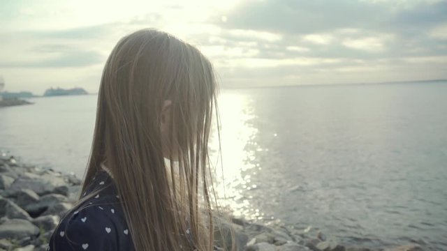 Nice small girl looking at golden sunpath at sunset at a sea in summer in slo-mo