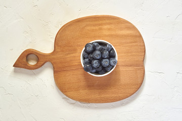 Top view of bowl with blueberries on wooden desk and white concrete background