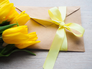 bouquet of yellow tulips on wooden background with envelope, tied with a ribbon space for text