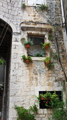 Fototapeta na wymiar Stone houses in narrow street of old town, beautiful architecture with arch and plants in pot, Trogir, Dalmatia, Croatia