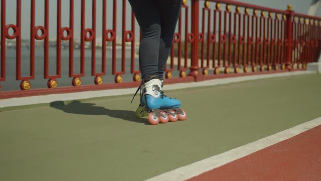 Close-up of young female feet in roller skates rollerblading forwards crossover and crisscross on river bridge. Woman roller enjoying outdoor riding along city footpath, street sport activity concept.