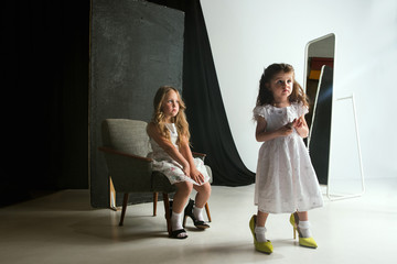 Interaction of children with adult world. Cute girls wearing mum's oversize shoes and dress for...