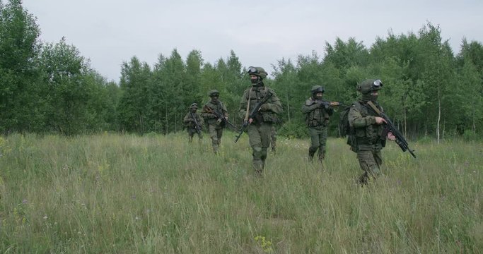 Soldiers in camouflage with assault rifle walking through the field military action in the steppe area, 4k slow motion.