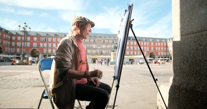 Skilled mature man painting in a public square in Madrid, Spain. Creative Spanish artist drawing with pencil on the street. People and creativity