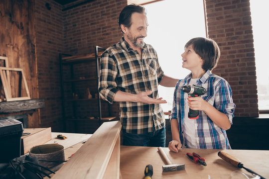 Portrait of two nice person cheerful woodworkers master handyman sharing experience skills showing how to use electrical device at modern loft industrial brick interior indoors