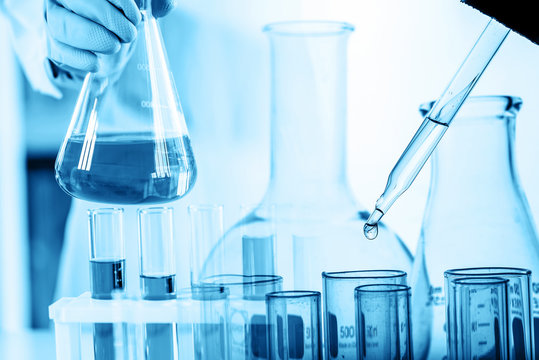 hand of scientist holding flask with lab glassware and test tubes in chemical laboratory background, science laboratory research and development concept