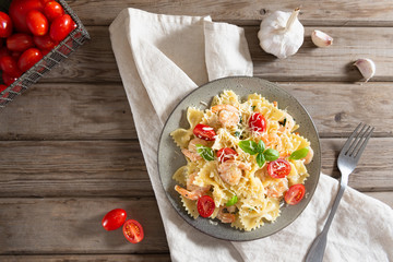 Italian pasta farfalle in a creamy garlic sauce with shrimps, cherry tomatoes and basil on a plate, top view. Copy space for text.