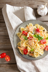 Pasta farfalle with shrimps, garlic sauce, cherry tomatoes and basil leaf on wooden table, italian cuisine, top view. Close up, copy space