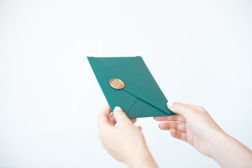 Close-up photo of female hands holding a green invitation envelope with a wax seal, a gift certificate, a postcard, a wedding invitation card