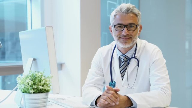 Mature doctor sitting at desk looking at camera