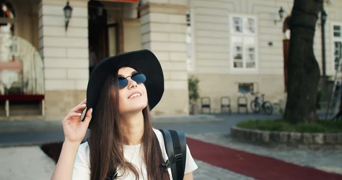 Beautiful female tourist in hat and eyeglasses taking photo of landmarks on smartphone