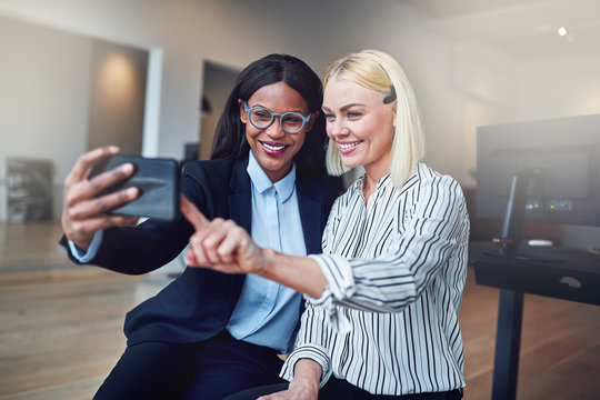 Two young businesswomen stadning in an office taking selfies tog
